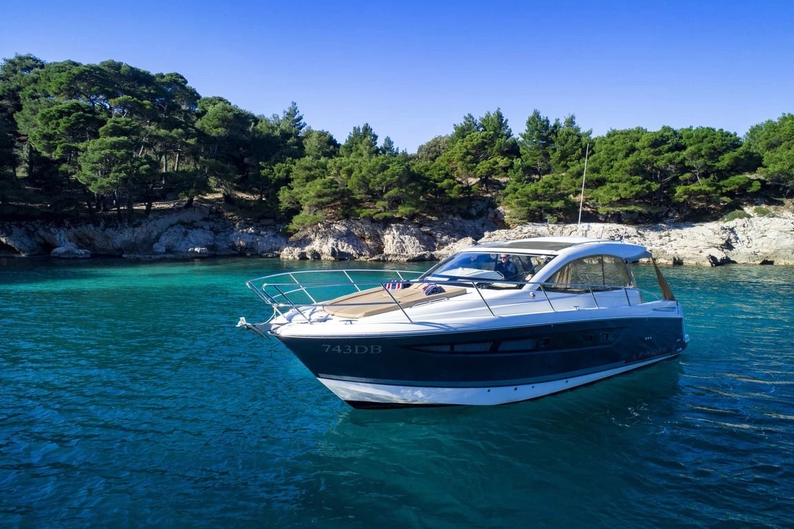 Jeanneau Leader 10 lying at anchor in a turquoise cove ringed by pines and white rock