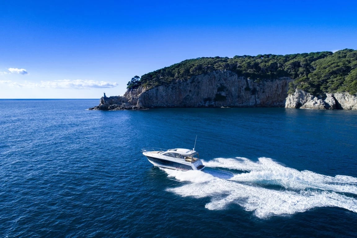 Aerial view of the Jeanneau Leader 10 trailing a white wake beneath a wooded headland