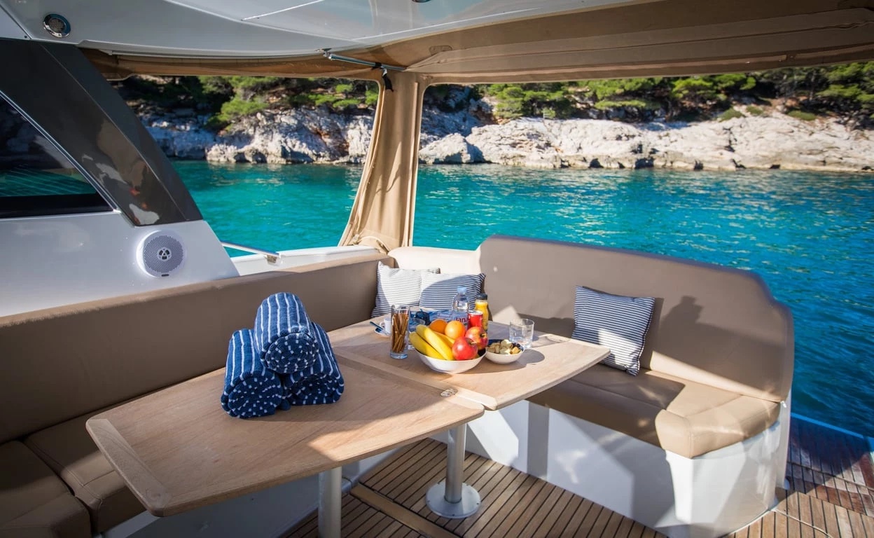 Aft-deck table on the Jeanneau Leader 10 laid with fruit, drinks and rolled striped towels in a quiet cove