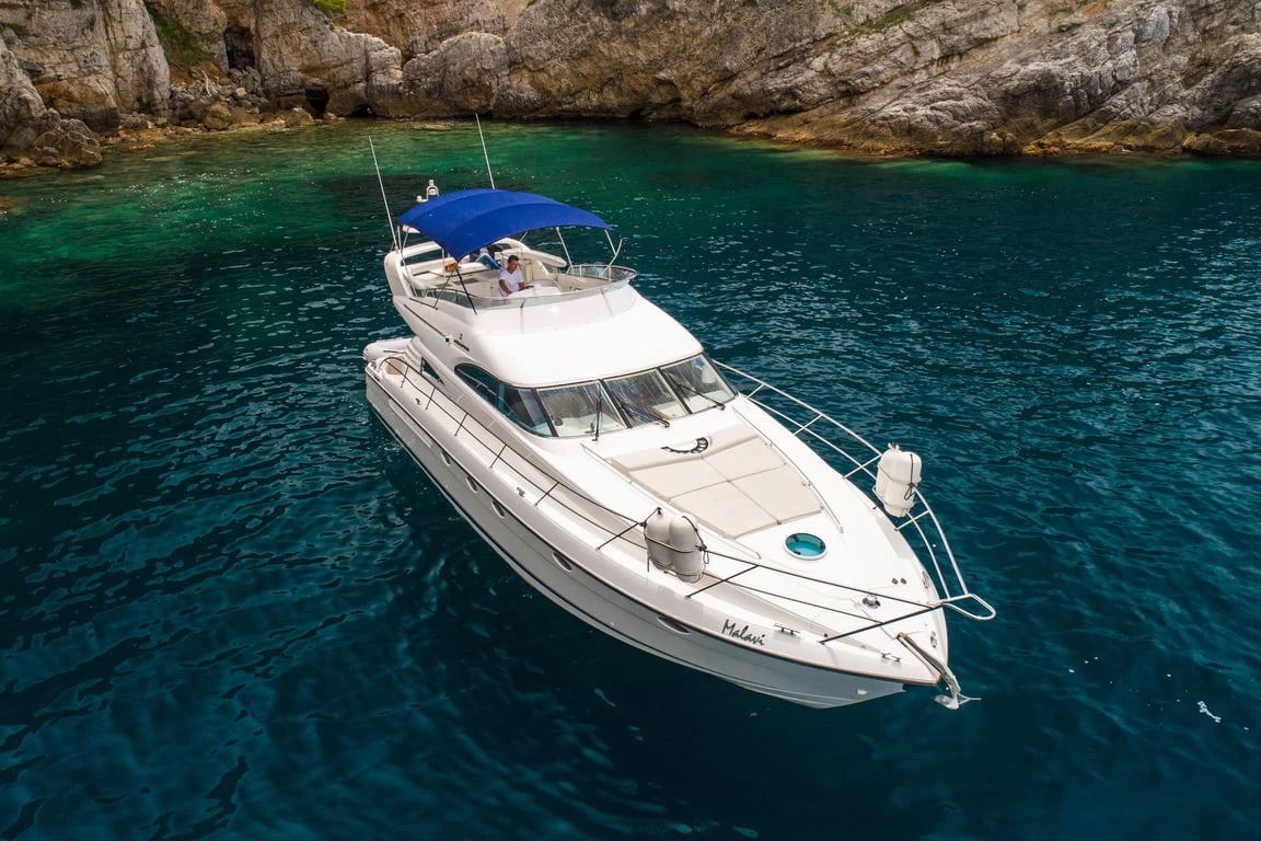 Malavi 55 anchored bow-on in a turquoise cove beneath rock cliffs, sun pads on the foredeck