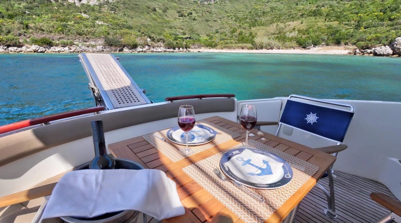 Cockpit table on the Prestige 440 Fly set with wine and anchor-motif plates, gangway extended towards a turquoise bay