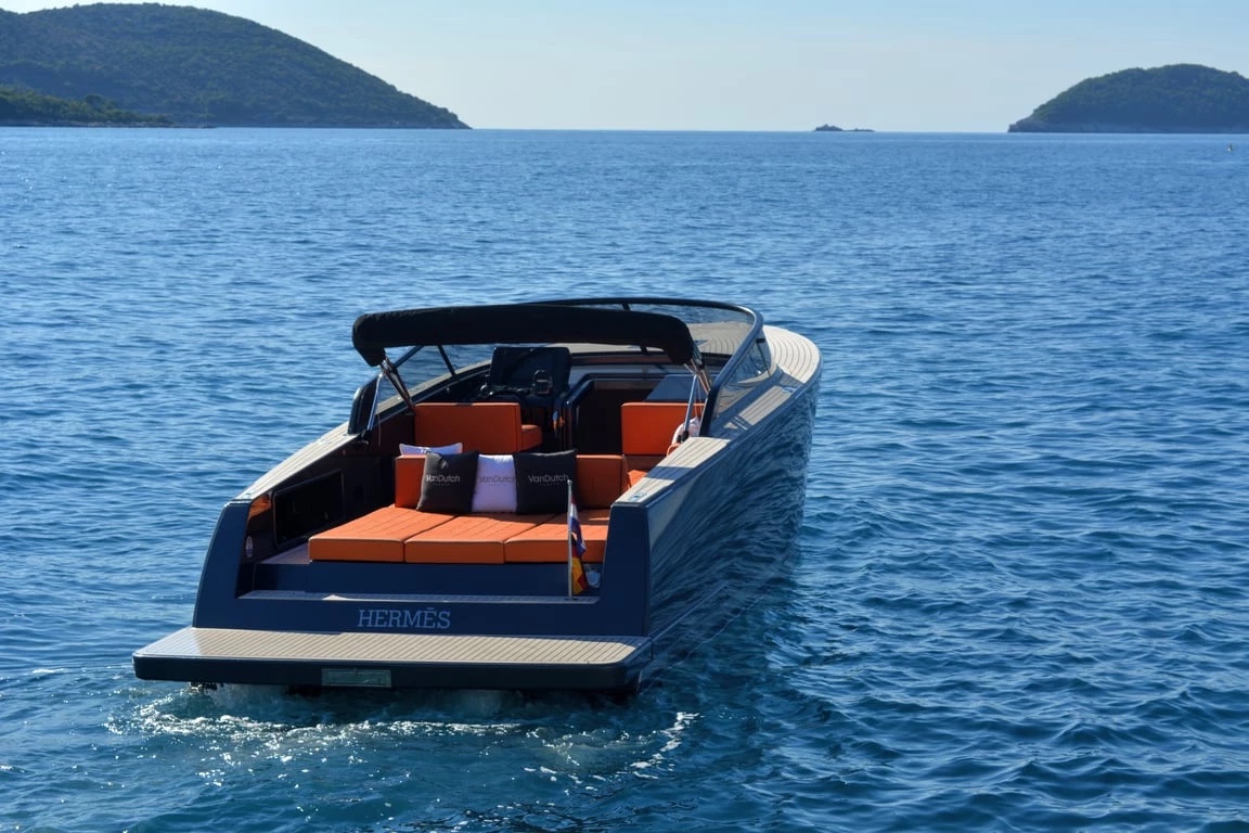Stern view of the VanDutch 32 at anchor — orange aft sun-pad, VanDutch cushions and teak platform, Hermès on the transom